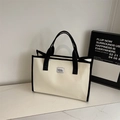 Detalle de un bolso tote de lona beige con asas negras sobre superficie de mármol - Blanco Roto