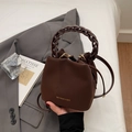 Detail of a brown matte bucket bag with gold lettering and woven chain handle - Coffee