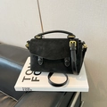 Detail view of black suede crossbody bag with gold hardware on a decorative book - Black