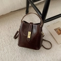 Dettaglio borsa a secchiello vintage in pelle cerata con chiusura oro su tappeto beige - caffè
