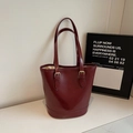 Detalle del bolso tote burdeos con textura brillante y hebillas metálicas doradas - Burdeos