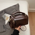 Deep brown box-style satchel bag with top handle and gold hardware on a gray blazer - Coffee