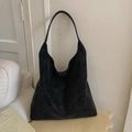 Close-up of minimalist black suede hobo bag with a subtle gold logo on a wooden surface - Black