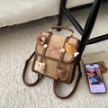 Detalle de mochila vintage marrón con colgantes de comida de peluche y un lazo - Caqui