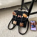 Detalle de una mochila de ante negro con colgantes de peluche y un lazo de cuadros - Negro