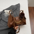 Detail einer braunen Falten-Tasche mit goldenen Beschlägen und einem Plüschkugel-Anhänger - Mit Anhänger / Braun