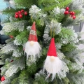 Dettaglio di gnomi natalizi in peluche appesi a un ramo innevato con bacche rosse vivaci - Set da 2