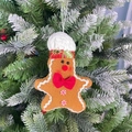 Detalle de un adorno de hombre de jengibre de felpa colgado en un árbol de Navidad nevado - Adorno Hombre de Jengibre Masculino