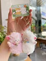 Close-up of pink and white plush lamb pendants with gold bell chains and gift tags - Lamb