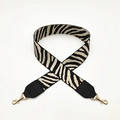 Macro detail of zebra pattern woven bag strap with golden lobster clasps and black leather ends - Beige and Black Leather