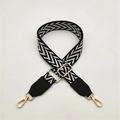 Close-up of adjustable woven black and white diamond pattern bag strap with gold lobster claw clasps - Black