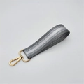 Close-up of gray woven wrist strap with silver reflective stripes and gold lobster clasp - Gray