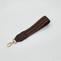 Macro view of geometric jacquard bag strap with brown leather and gold lobster clasp - Brown