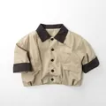 Detail van een beige kinderjasje met bruine kraag en grote zakken in een neutrale stijl - 80cm / Licht kaki
