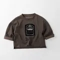 Detail view of cotton kids long sleeve tee with roll-edge hem and artistic chest patch - 80cm / Coffee