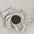 Detail eines grauen Mädchen-T-Shirts mit einem schicken dunklen runden Aufnäher - 80cm / Beige Aprikose