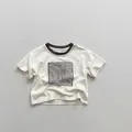 Dettaglio della maglietta per bambini in cotone crema con bordino marrone e stampa - 80cm / Beige