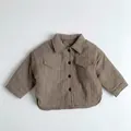 Detalle de chaqueta acolchada marrón para niños con textura plisada y bolsillos de parche - Caqui / 90cm