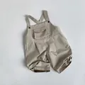 Detail of light beige cotton kid's overalls showing decorative chest pocket and texture - Beige Apricot