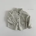 Dettaglio di camicia cargo verde chiaro per bambini con tre tasche e bottoni scuri - 80cm / Grigio Beige