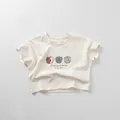 Detail eines Baby-Baumwoll-T-Shirts mit Apfelprints und Slogan auf cremefarbenem Stoff - 80cm / Beige Aprikose