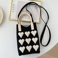 Close-up of black knit phone bag with white heart patterns and beige curved handle - Heart Pattern Black