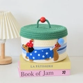 Dettaglio di un cesto intrecciato con ricamo a bassotto e coperchio verde per neonati - Stile Cane Blu con Coperchio Verde