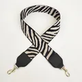 Dettaglio della tracolla larga zebrata nera e bianco sporco con ganci dorati - Nero + Beige