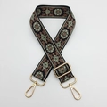 Close-up of ethnic style embroidered strap with floral patterns and golden metal clasps - Black Background Green Edge Brown