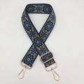 Close-up of ethnic embroidered bag strap with floral patterns and gold metal swivel hooks - Black Background Blue Edge Beige