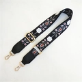 Detail view of ethnic embroidery on adjustable black bag strap with gold metal hooks - Black Floral Plant + Black