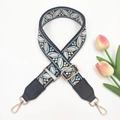 Detail of adjustable wide shoulder strap with blue floral embroidery and gold metal hardware - Black Background Light Blue
