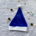 Close-up of blue plush Christmas hat with white pom-pom on faux fur rug with pinecones - Blue