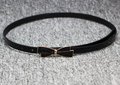 Detail of thin black patent leather belt with a golden bow buckle on grey background - Black