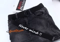 Detail eines schwarzen Stoffgürtels mit D-Ringen und weißem Schriftzug auf grauem Denim - Schwarz