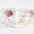 Detail of heart-shaped cutout metal waist chain in golden finish on a magazine - Gold Heart Waist Chain