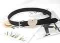 Detail of a thin black leather belt featuring a large polished silver heart buckle ornament - Black