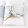 Detail view of a white leather thin belt with a gold rope textured metal buckle on a magazine - White