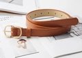 Dettaglio cintura in pelle marrone con fibbia a D dorata su rivista di moda - Cammello