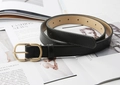 Dettaglio di cintura nera minimalista con fibbia ovale in oro opaco su rivista di moda - Nero