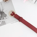 Stijlvolle bordeauxrode lederen riem met een gouden ronde gesp in lifestyle-decor - Bordeauxrood