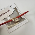 Close-up of red thin leather belt with gold metal flower buckle and white pearl details - Red