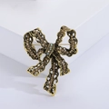 Vintage gold alloy bow brooch featuring brown rhinestones on a white display block - Gold