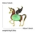 Spilla pegaso dorata con opale verde e strass arancioni su sfondo bianco puro - Oro con pietra occhio di gatto verde
