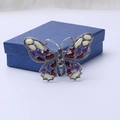 Detalle de broche de mariposa plateado vintage con cristales púrpuras en caja azul - Morado