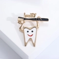 Close-up of a creative white tooth enamel pin with a golden toothbrush and healthy text - Gold-Black
