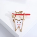 Macro shot of a cartoon tooth brooch with a red toothbrush and healthy text detail - Gold - Red