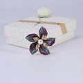 Dettaglio di una spilla a fiore con perla e petali sfumati su scatola regalo bianca - Viola