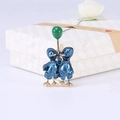 Detail of enamel duck pins with a green balloon placed against a textured gift box - Blue