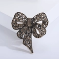 Macro detail of vintage bronze bow brooch with amber rhinestones and filigree texture - Brown